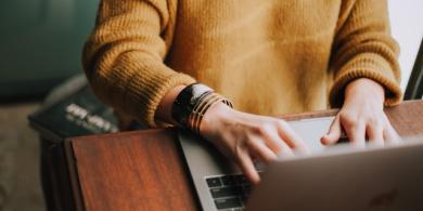 Person typing on a laptop wearing a mustard sweater.