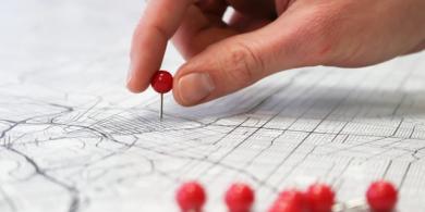 Hand placing a red pushpin on a map.