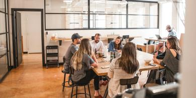 Coworkers sit around a wooden table in a modern office.