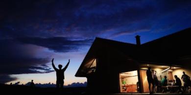 People gathered at a cozy cottage during twilight, enjoying the evening outdoors and indoors.