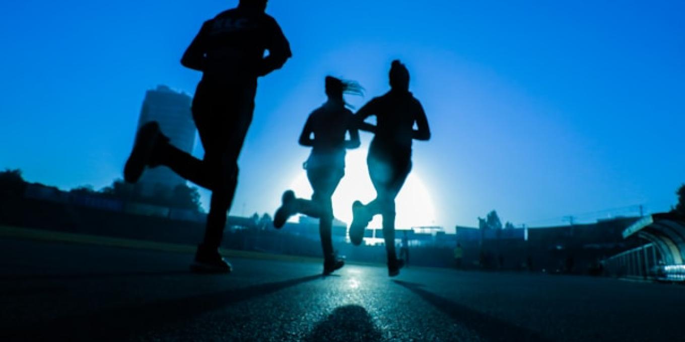 Silhouettes of three people running at sunrise on a track.