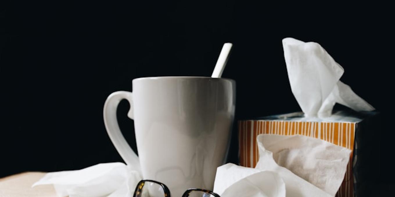 Mug with straw, tissues, and glasses on a table against a black background.