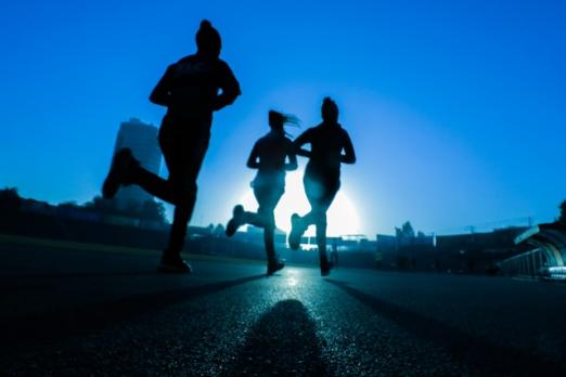 Silhouettes of three people running at sunrise on a track.