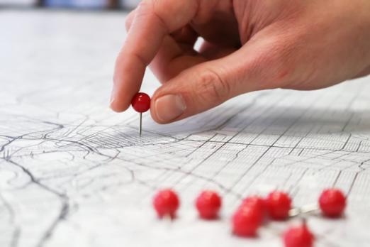 Hand placing a red pushpin on a map.