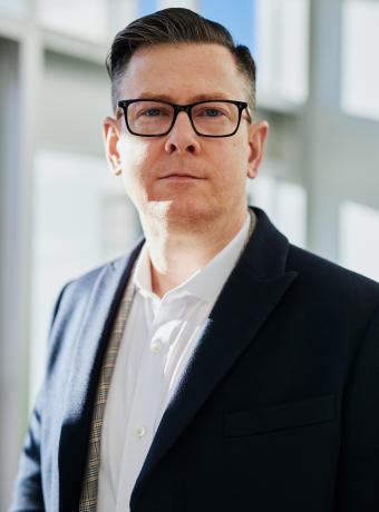 Man in suit and glasses standing in bright office setting.