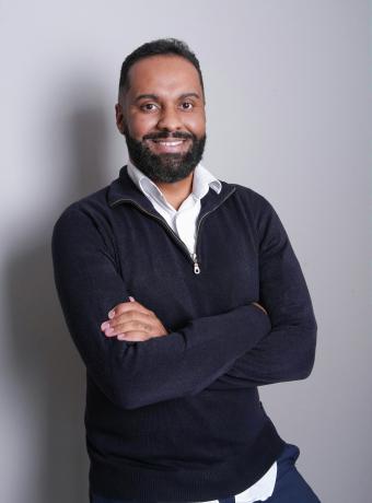 Smiling man with a beard, arms crossed, wearing a black sweater.